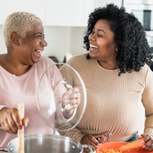 Happy Afro mother and daughter preparing lunch together in modern house kitchen - Food and parents unity concept