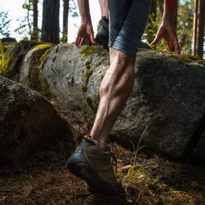 Muscled leg of the trail running athlete crossing rocky terrain in the summer forest