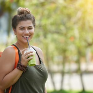 Portrait of joyful young sporty woman drinking smoothie after practicing outdoor yoga